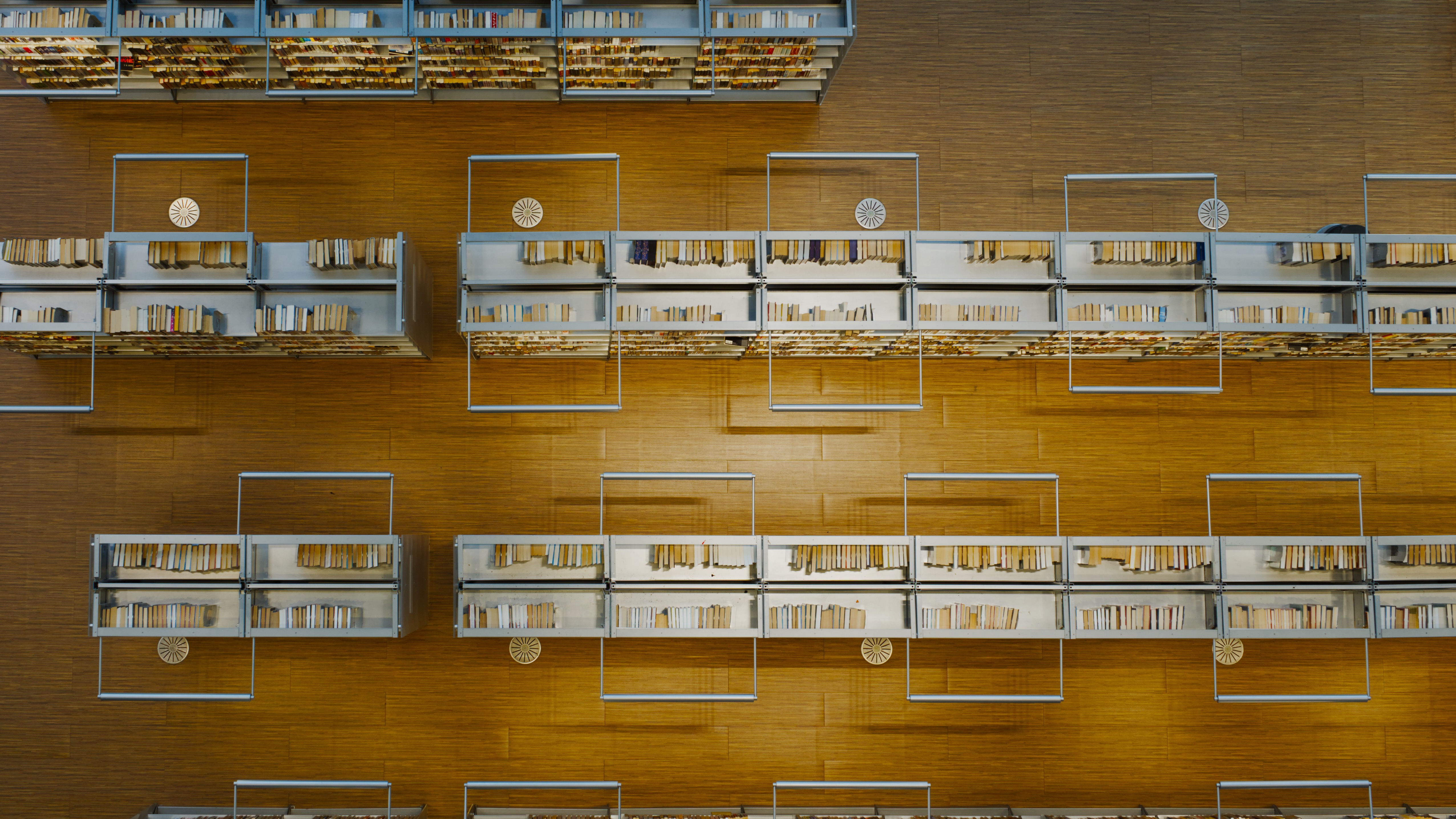 Overhead view of a library floor with wooden shelving units displaying books arranged horizontally and vertically.